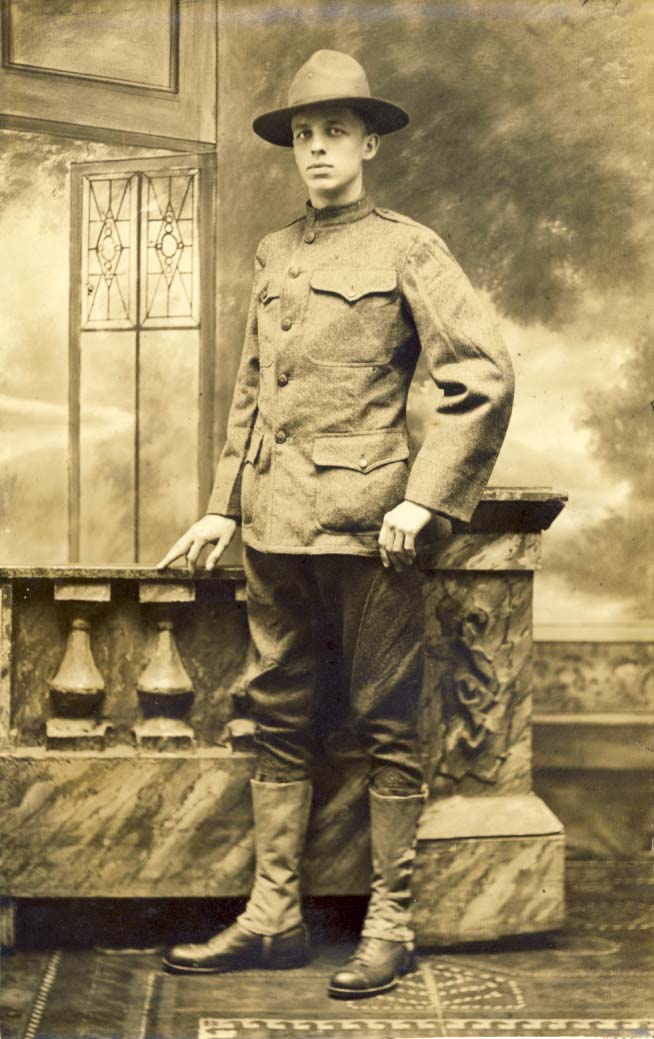 U.S. soldier, wearing hat and jacket, hand on rail; studio photo postcard