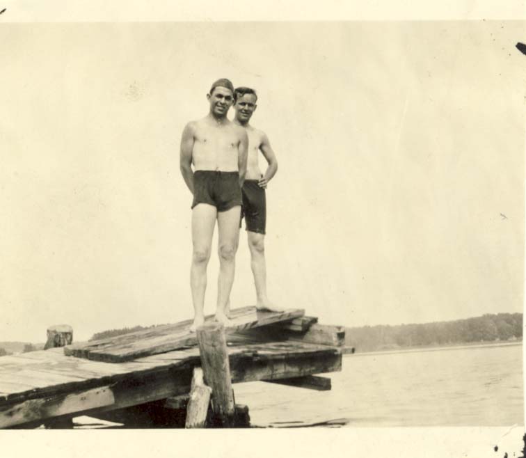 Two men in bathing suits standing on dock on lake photograph