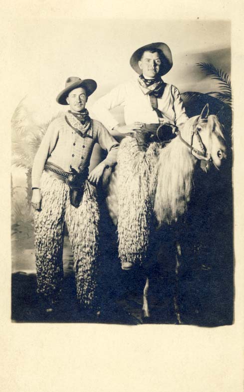 2 men, both in chaps, one on fake horse postcard
